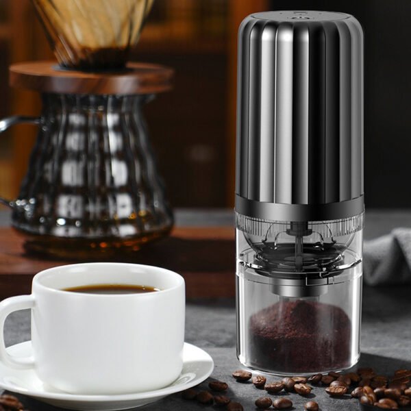 Black portable coffee grinder next to a cup of freshly brewed coffee and a pour-over kettle