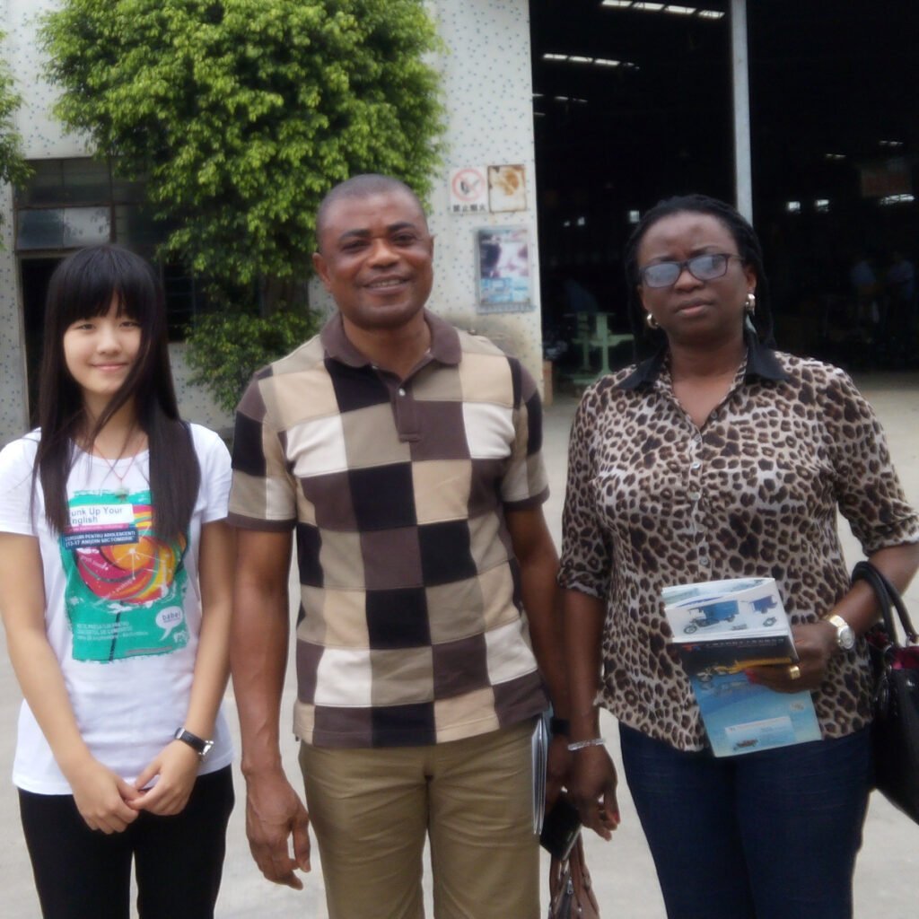 Tiny’s Work with Ghana Clients Tiny with her clients from Ghana at a three-wheeler motorcycle factory, showcasing her early global sourcing experience.