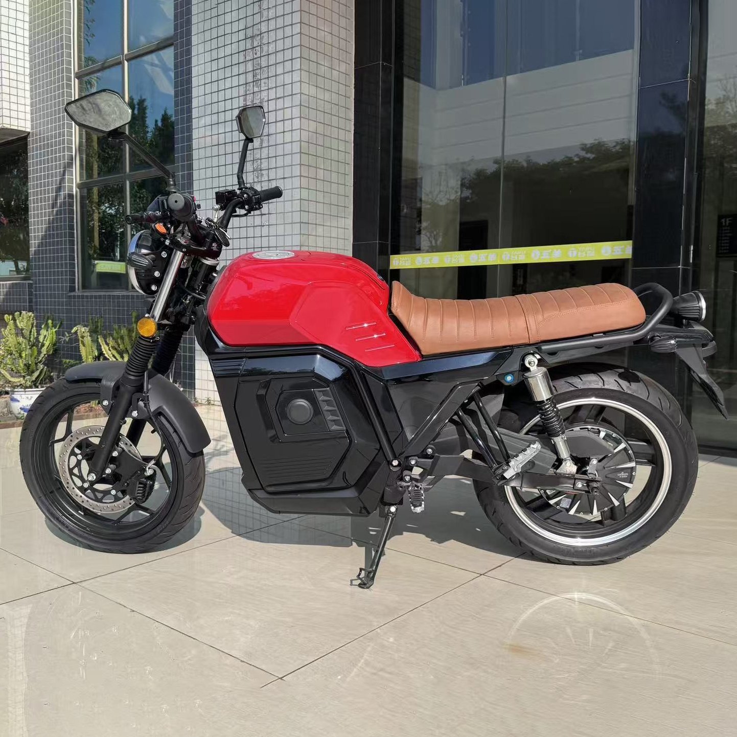 Red electric motorcycle with brown seat, round headlight and black body panels, shown from a front three-quarter angle